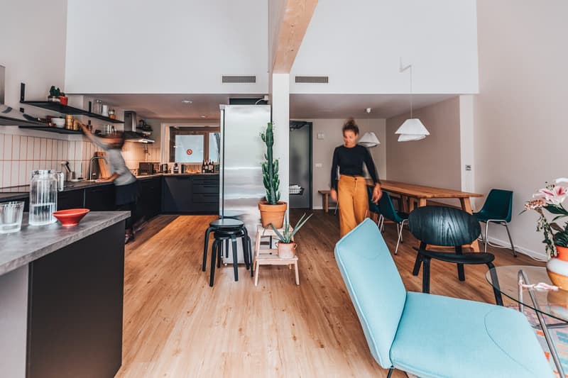 an open plan kitchen, living, and dining area with wooden floors, various furniture, and potted plants, with a view of a hallway