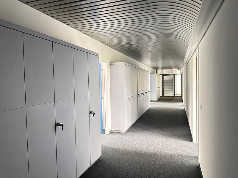long hallway with carpeted floor, rows of lockers on each side, arched ceiling, glass doors leading to another room