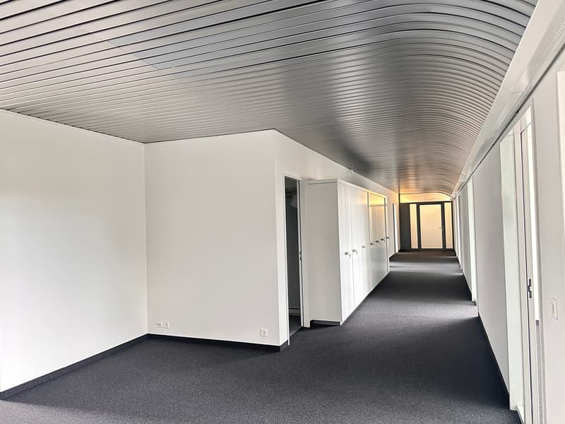 wide corridor, white walls, gray ceiling, white tile floor, closed doors, electrical outlets