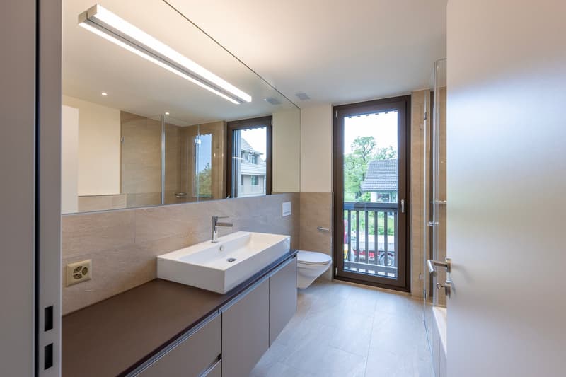 modern bathroom with large mirror, white sink, toilet, glass door to balcony