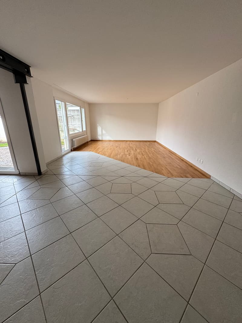 Empty room with white tiled floor, large windows, sliding door leading to balcony, wooden floor