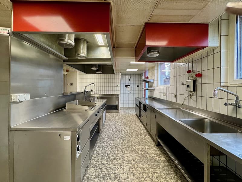 large stainless steel kitchen, with cooking stoves, grill, sinks, cabinets, white tile walls, extractor hoods, lights