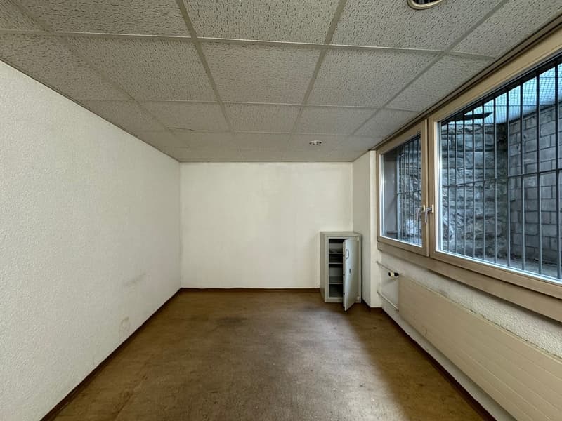 empty room with a wooden floor and white walls, an open metal safe, a metal radiator, a window with iron bars