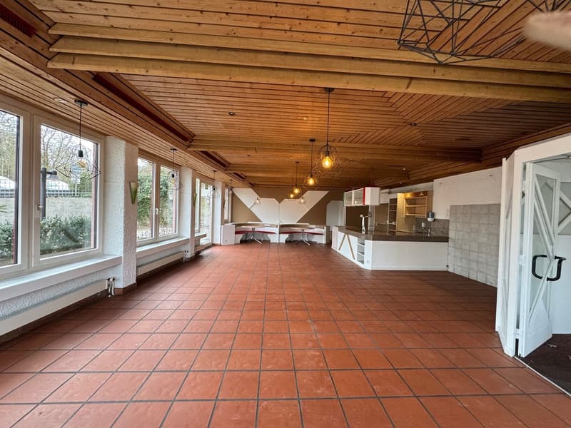 Spacious room with wooden beams ceiling, tile floor, kitchen island, and big windows.