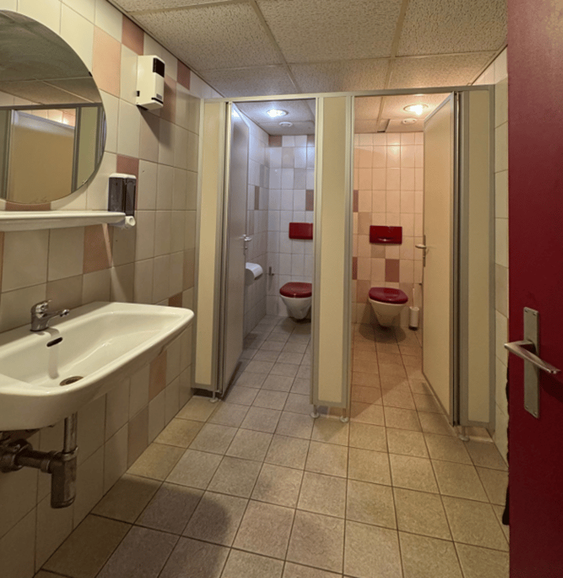 Public restroom with tiled walls and floor, a sink, a mirror, and two toilet stalls.