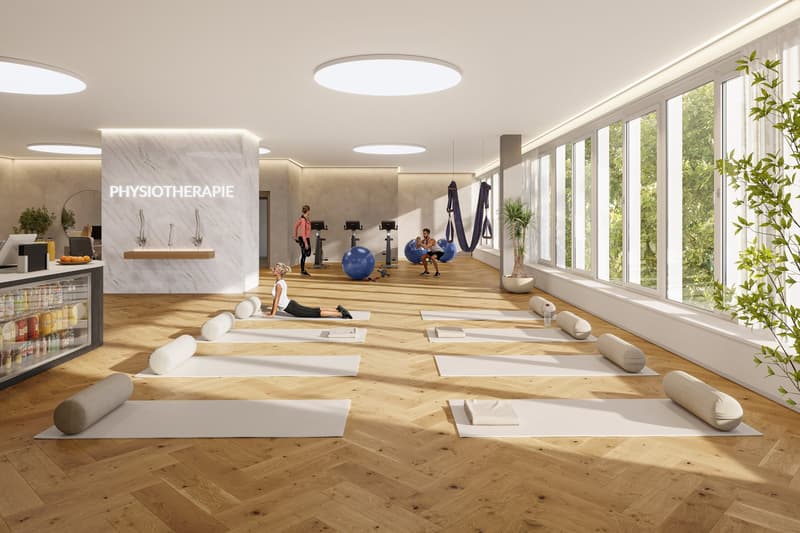 Large open space with hardwood floors, floor-to-ceiling windows, physiotherapy equipment such as exercise balls and suspension straps, and a sign indicating this is a physiotherapy room
