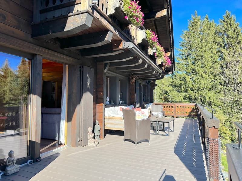 wooden chalet, glass doors, balcony with wooden railing, furniture on balcony, outdoor plants, outdoor statue