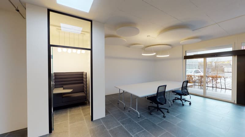 Office room with a long table, three chairs, a cushioned sofa, glass door, suspended lights.