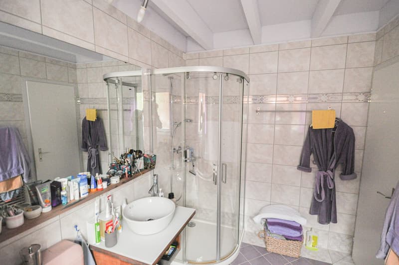 walk-in shower, vanity, basket of towels, robes hanging on the wall, mirror, toiletries on counter