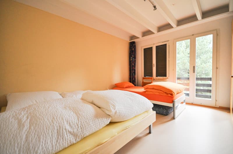 Two wooden single beds, yellow floor, orange bed spread, white curtains, sliding glass door.
