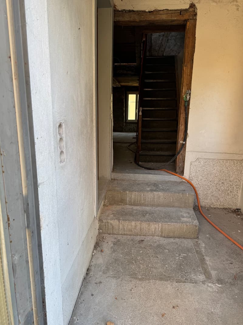 a concrete corridor with two steps leading up to a doorway, white walls, orange hose on the floor
