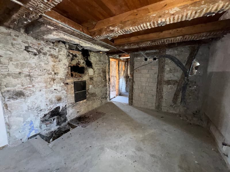 Old room with stone walls, exposed wooden ceiling, wires, and some damages on the wall