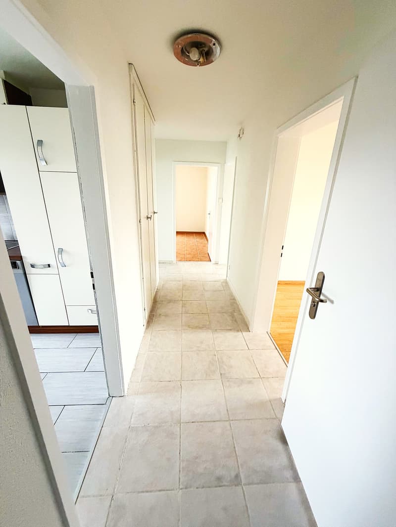 Empty hallway with tiled floor, white walls, and doors leading to different rooms.