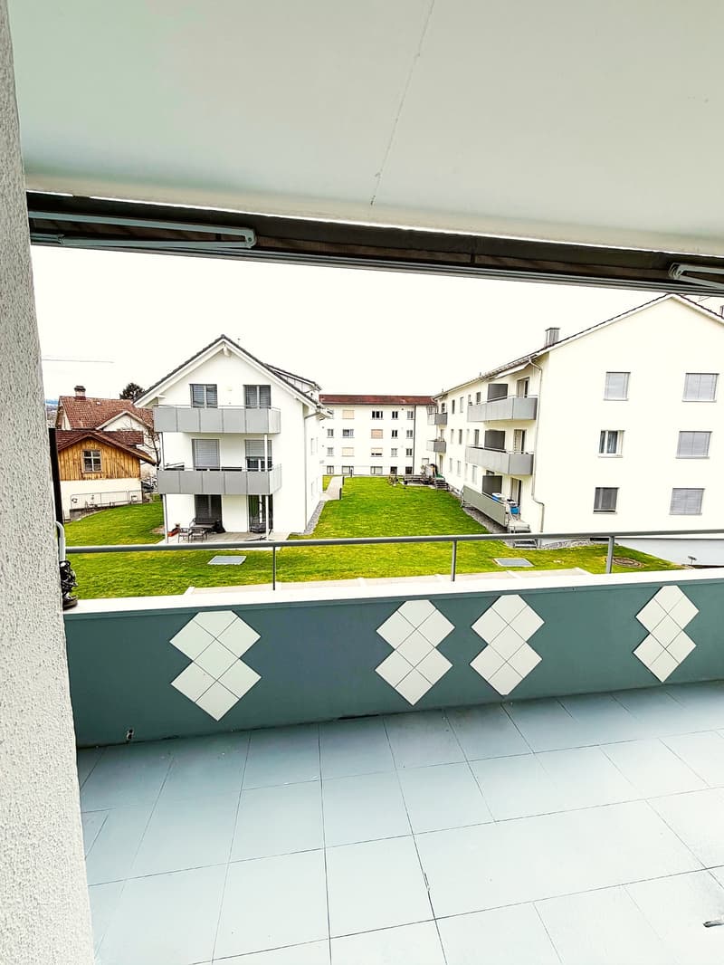 Balcony with tiled floor, metal railing, view of a grassy area and buildings