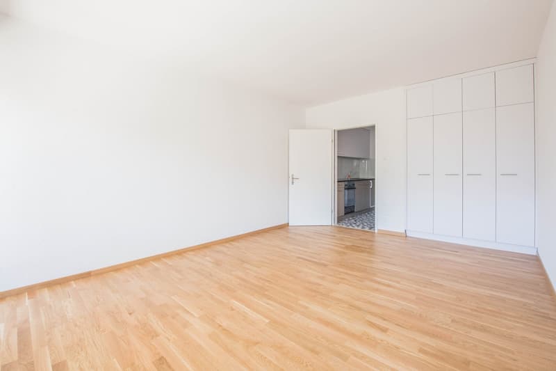 empty room, wooden floor, white walls, white cabinets, open door to kitchen