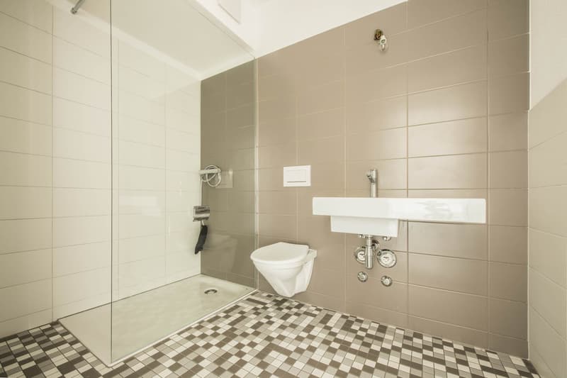 Modern bathroom with glass shower enclosure, white toilet, white sink, tiled floor, tiled walls