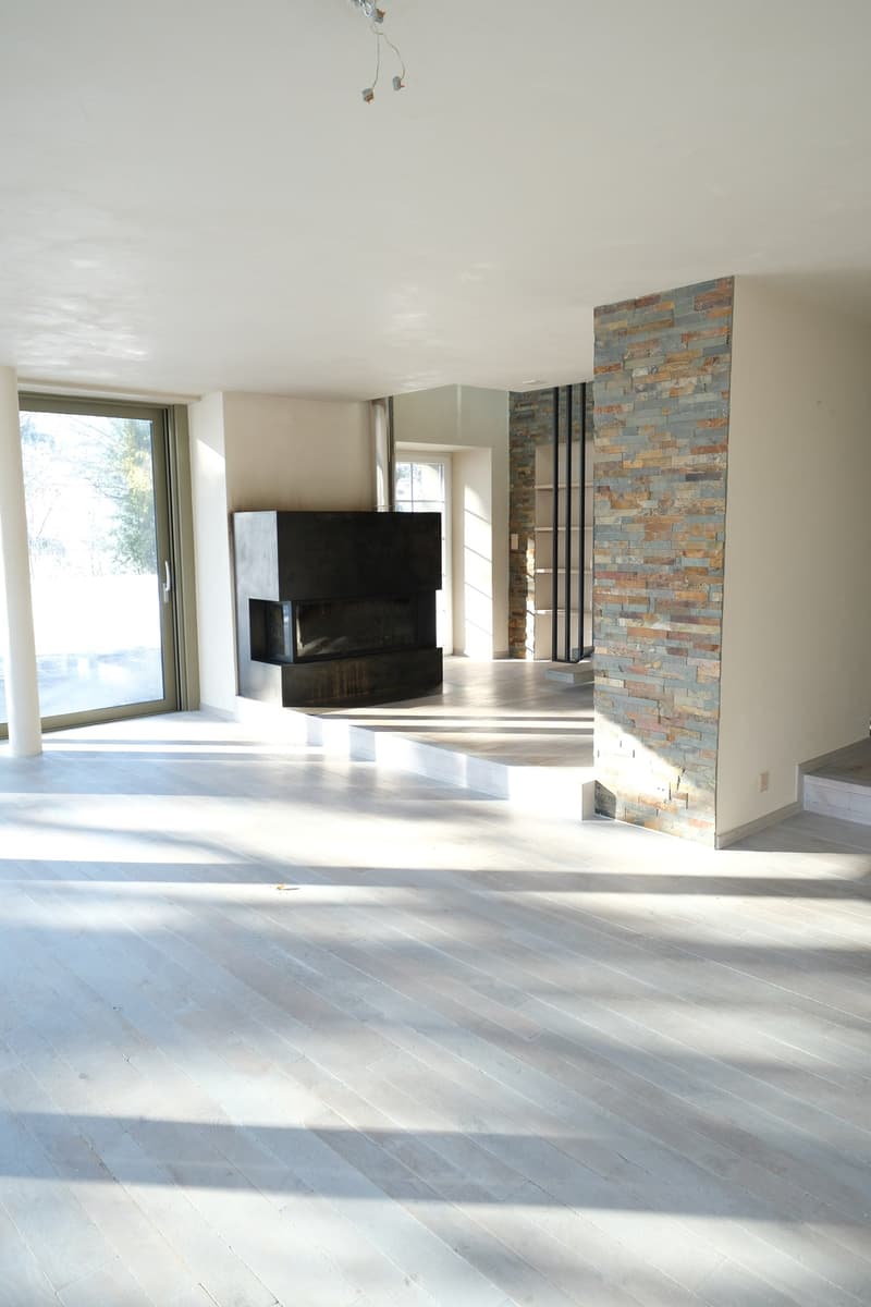 Spacious living room with large windows, hardwood flooring, and a stone fireplace feature wall