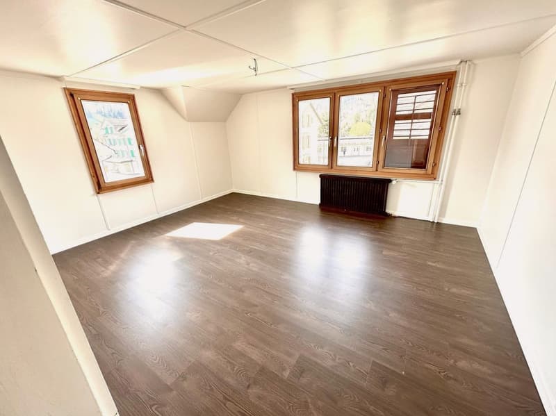 Empty room with wooden floor, two windows, white walls, and central heating radiator