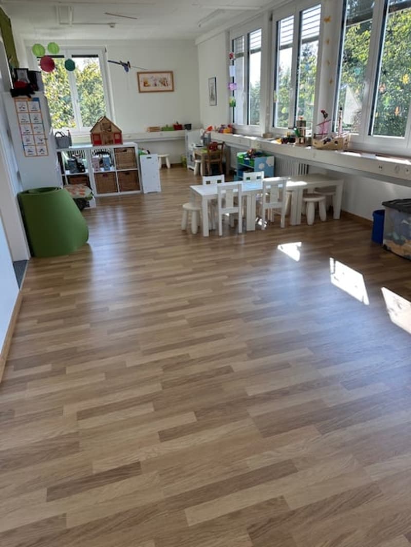 playroom with wooden floor, white walls, glass windows, toys, small tables and chairs, wooden house