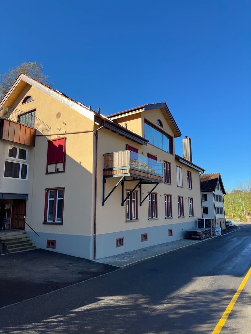Three-story building, beige exterior, multiple windows, balcony, chimney, stairs to entrance