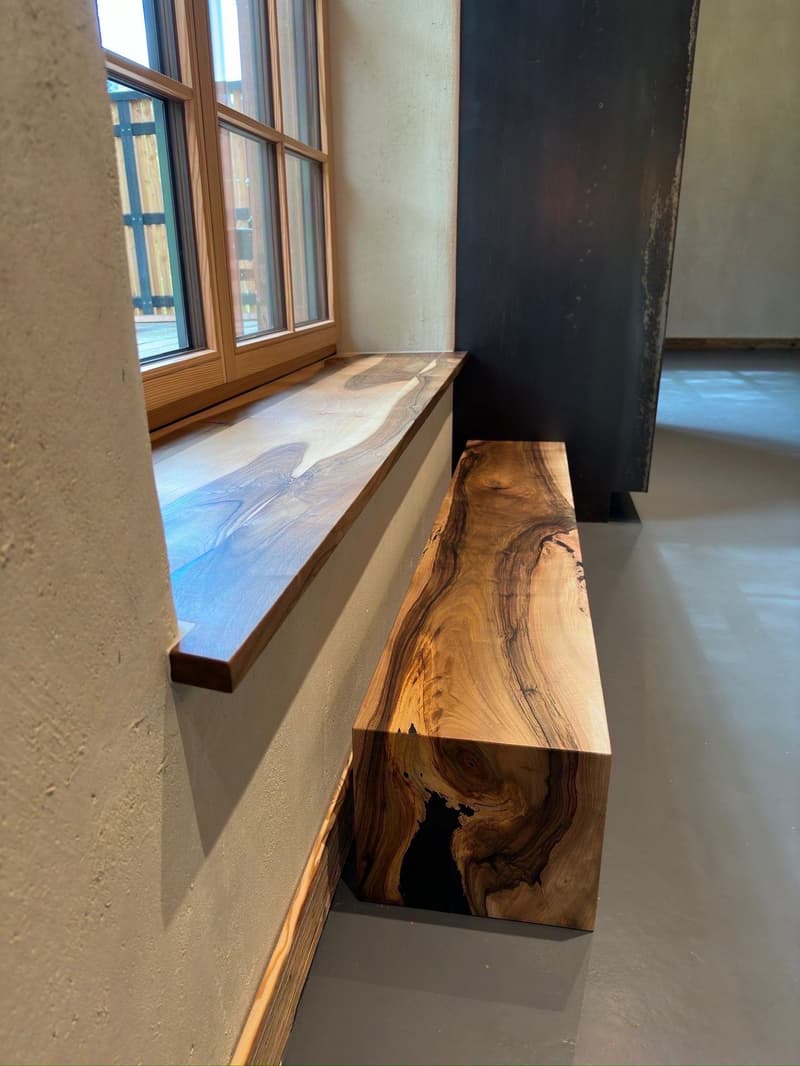 Wooden window bench with unique design and wooden floor next to a glass window.