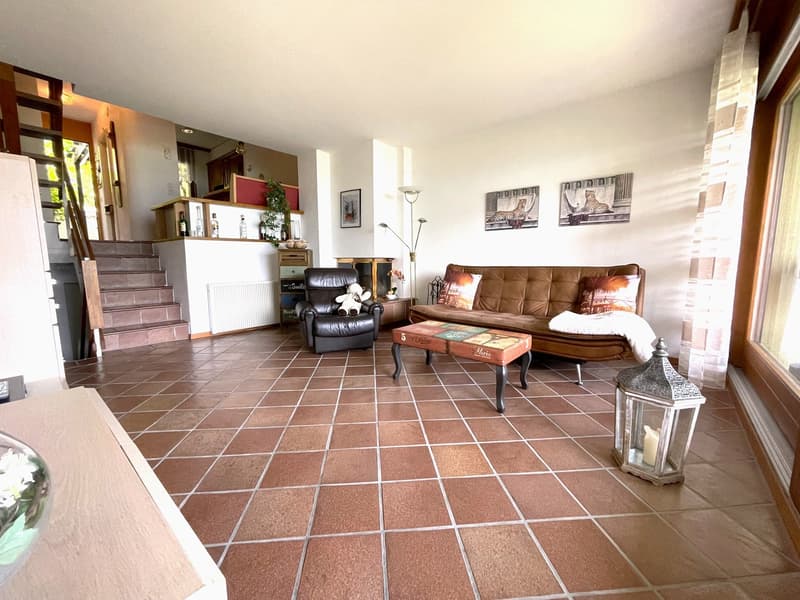 Spacious living room with tile flooring, leather sofa, armchair, coffee table, and decorative items. The room features a fireplace and built-in shelving units.