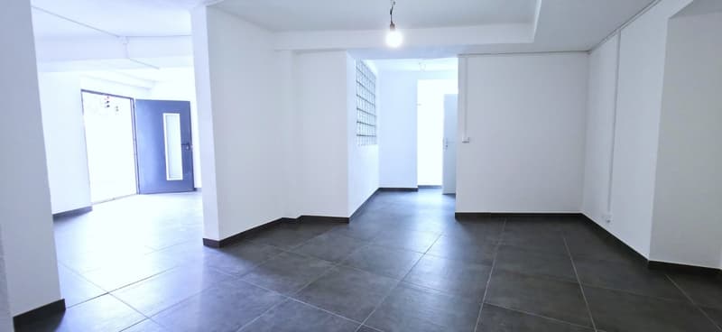 Empty room, white walls, black tiled floor, two doors, one with glass panel