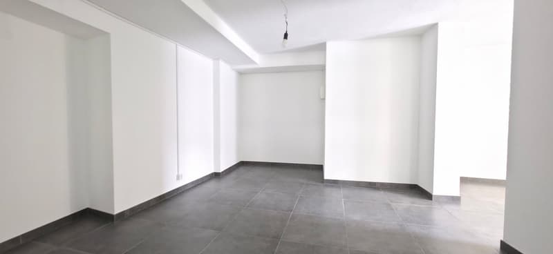 Empty room with white walls, gray tiles, and a ceiling light