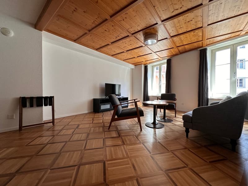wooden floor, wooden ceiling, white walls, flat screen TV, wooden desk, two chairs, two couches