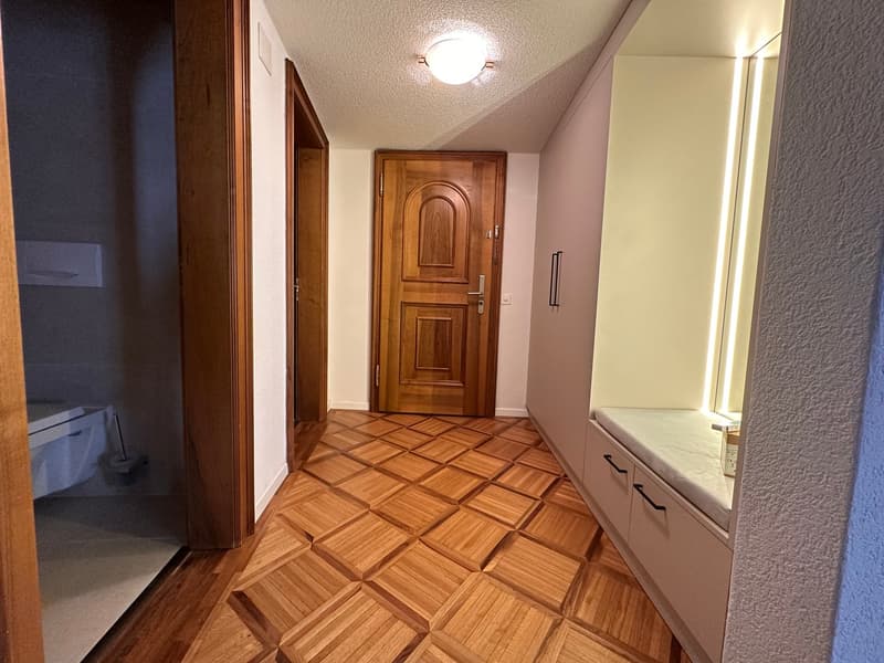 long hallway with parquet flooring, closed wooden door, wooden drawers, bench, light fixture