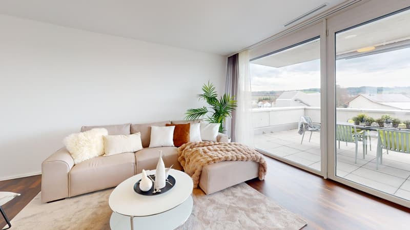 Large windows, balcony with chairs, table, couch with pillows, coffee table, rug, decorative plant, and white walls.