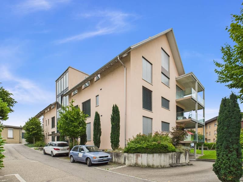 3 story apartment building, beige exterior, glass windows, balcony, 2 cars parked in front