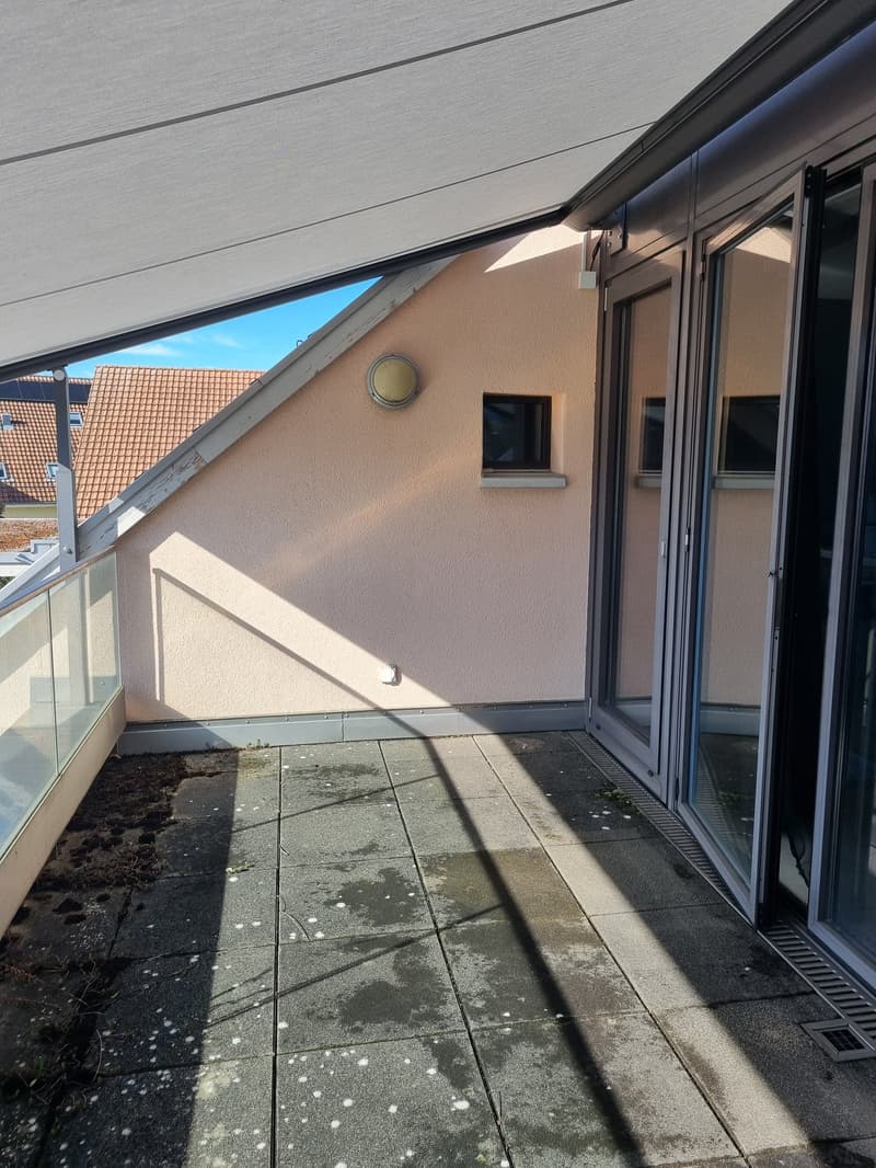 Balcony with glass railing, retractable awning, sliding glass doors, wall-mounted light fixture, small window