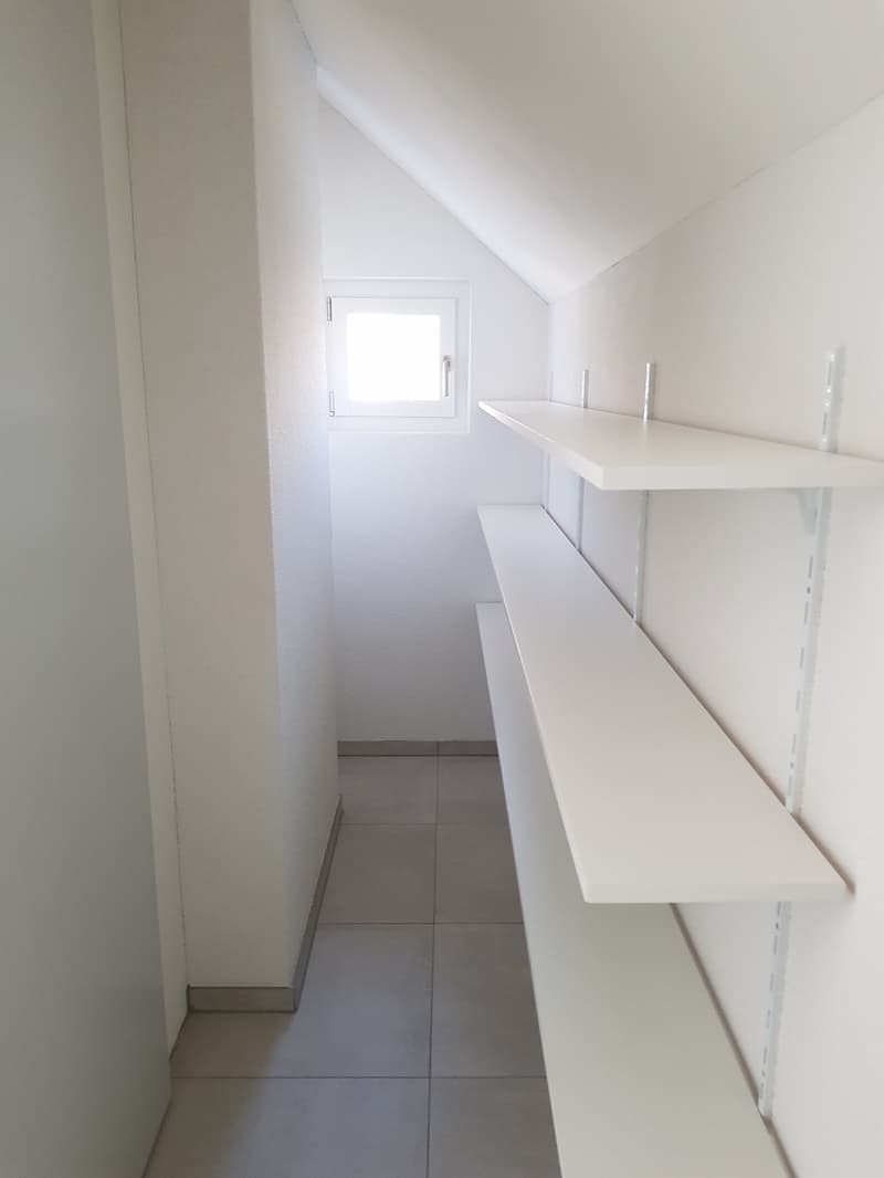 Empty room with white walls, tiled floor, and white shelves