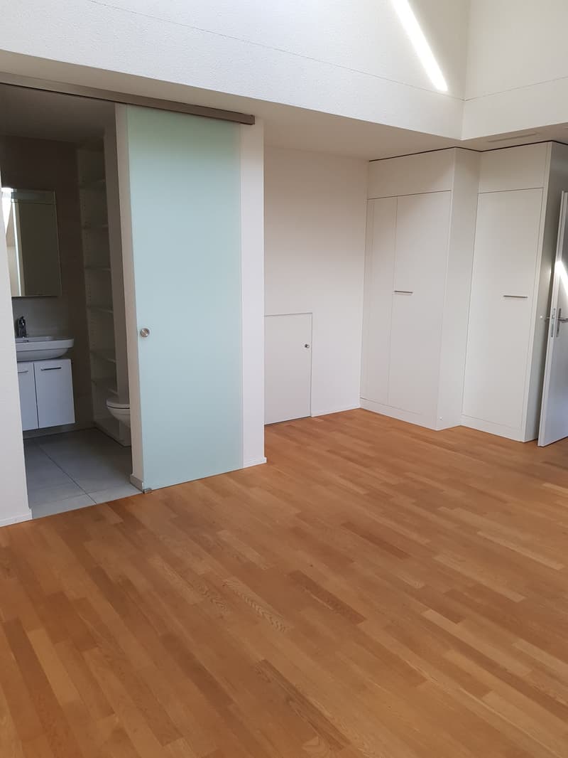 Empty room with wooden floor, white walls, sliding door, and a small bathroom with toilet and sink.