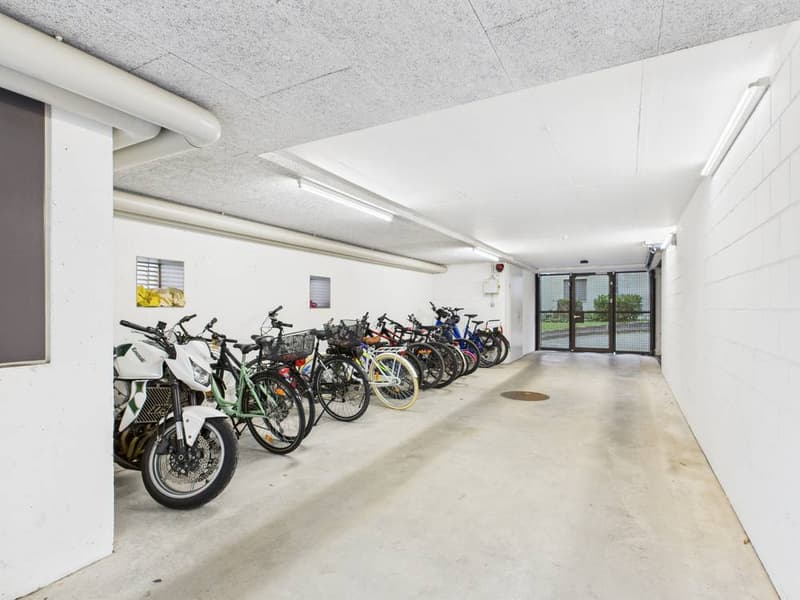 Underground parking area with multiple bicycles parked in a row, white walls, and ceiling lights