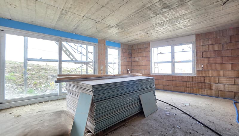 Empty room with large windows, stack of materials, unfinished walls