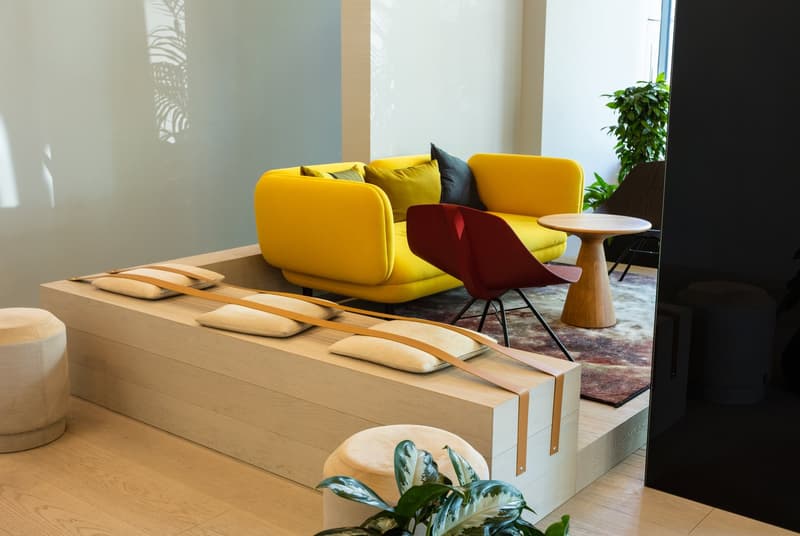 Bright and modern living room with a yellow sofa, red accent chair, wooden coffee table, and potted plants. The room features large windows and a fireplace, creating a cozy and inviting atmosphere.