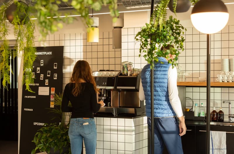 Modern kitchen with white tile walls, a modern coffee machine, sink with a faucet, and shelves with cups and bottles