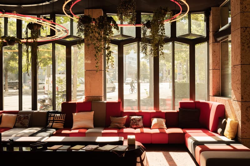 Large windows with a view of the street, red and brown sofas and chairs, hanging plants and decorations, modern and cozy interior design