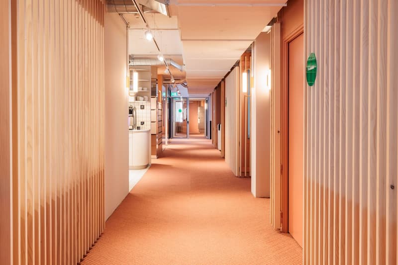 orange carpet, white walls, wooden paneling, illuminated by overhead lights, doorways, green signage, open door, kitchen area with appliances and counter