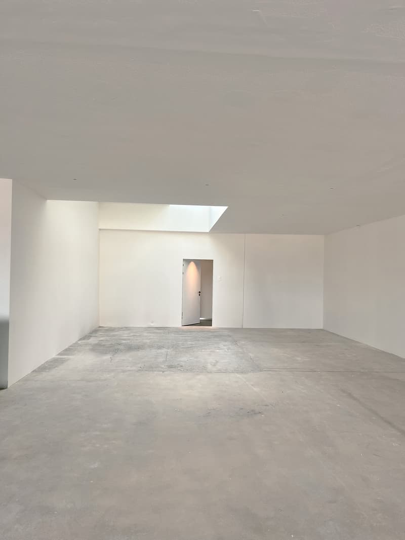 Large open space with white walls, concrete floor, and a doorway visible in the background.