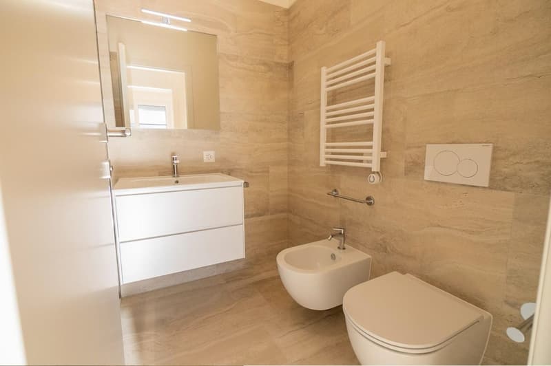 Spacious bathroom with beige marble-like tiles, a vanity unit with a sink, a toilet, and a towel warmer.