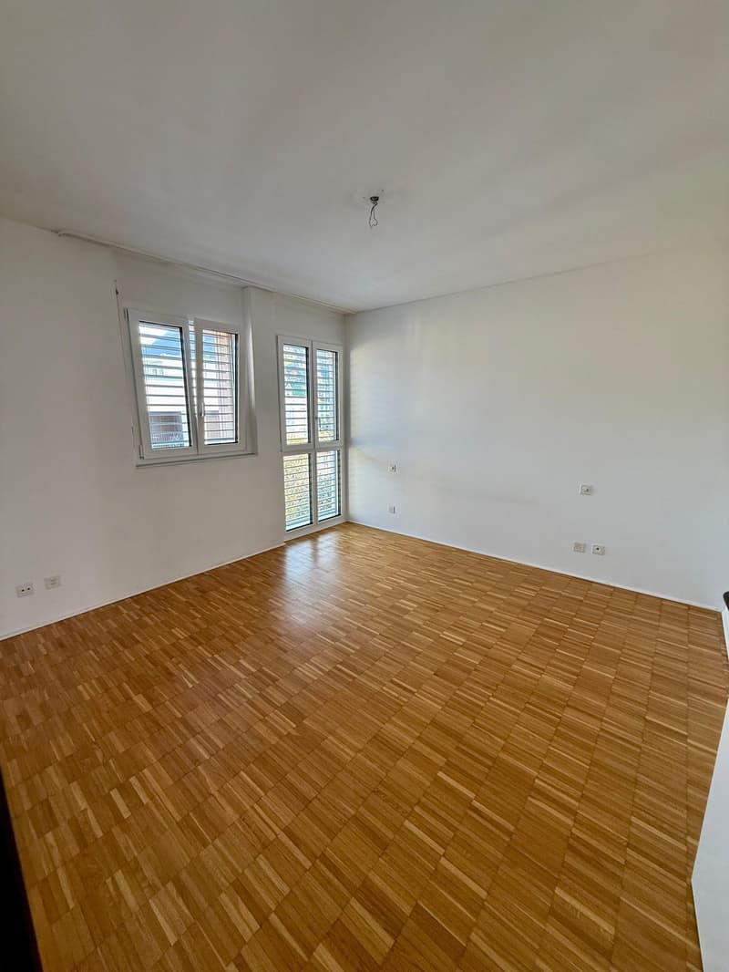 Empty room with wooden floors, white walls, two windows with shutters, power outlets