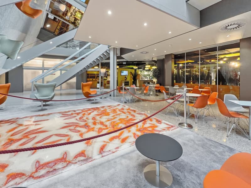 modern lobby with carpet, orange chairs, tables, staircase, glass walls, plants, monitor