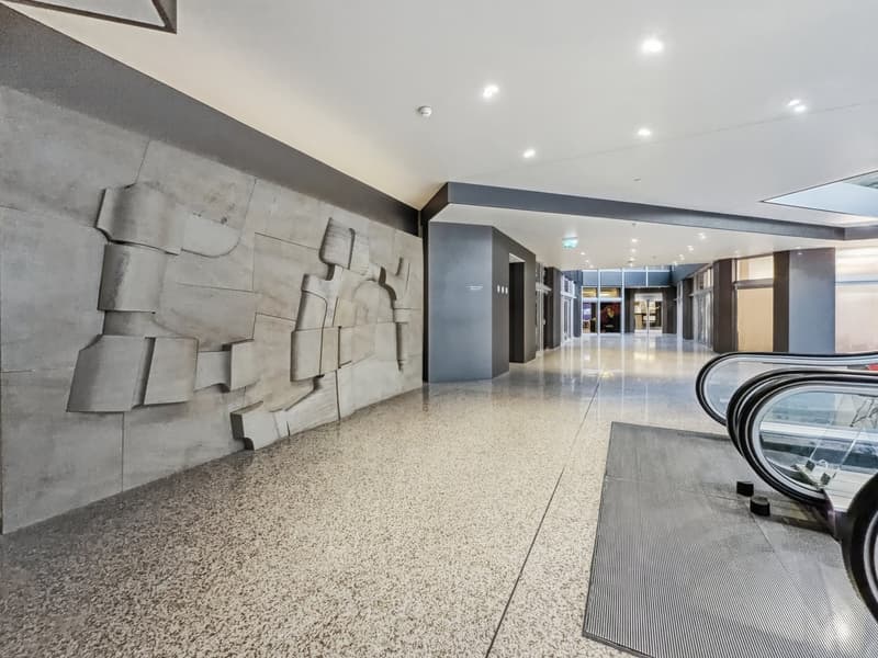 Concrete wall with abstract design, polished concrete floor, escalator, gray carpet, white ceiling with recessed lighting