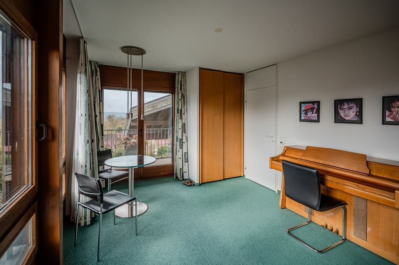 room with green carpet, wooden piano, glass table, chairs, glass door, balcony, curtains, picture frames