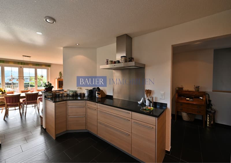 modern kitchen with wooden cabinets, black countertops, wooden floors, glass windows, and a large stove hood