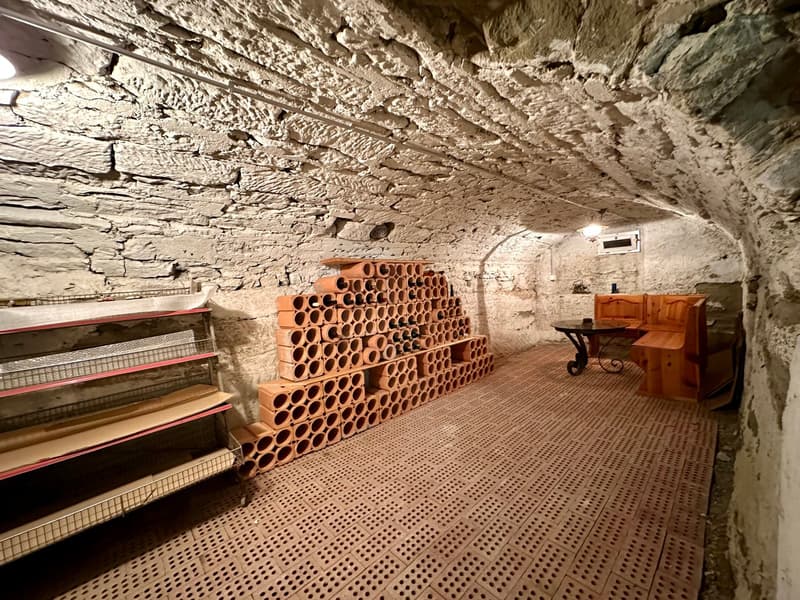Room with clay barrel storage, wooden shelves, wooden table, and benches.