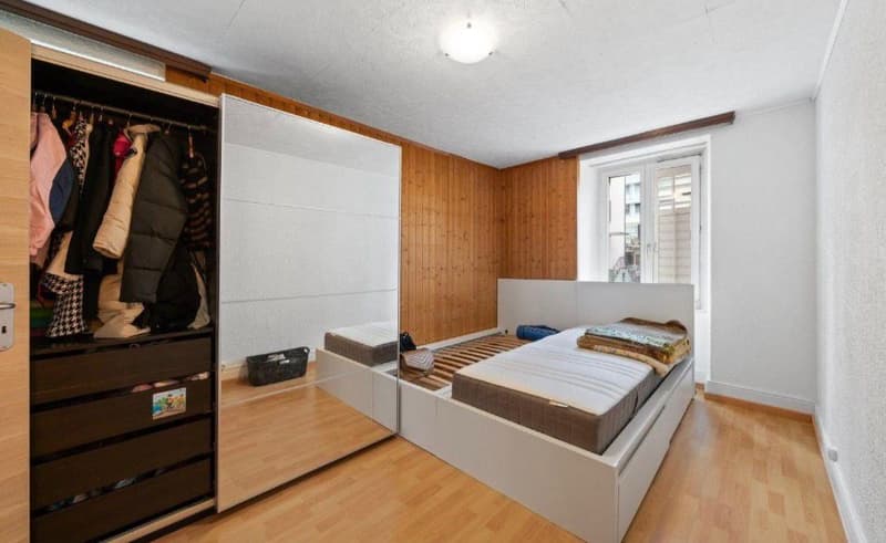 Bedroom with wooden floor, white walls, wooden paneling, large mirror, double bed, wardrobe with drawers, window with balcony access